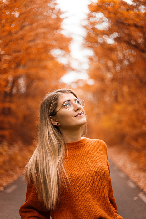 Beautiful autumn photography of a female model in orange posing in front of orange leaved trees 