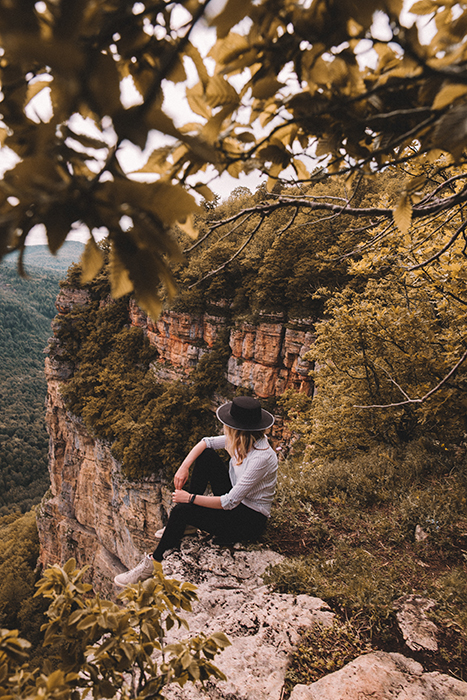 An outdoor portrait of a female model sitting on rocks amidst a beautiful mountainous landscape - fall photography tips 
